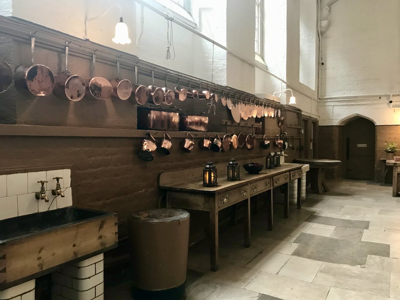 a look along the kitchen with a wooden sink, freestanding wooden table and copper saucepans hanging along the wall