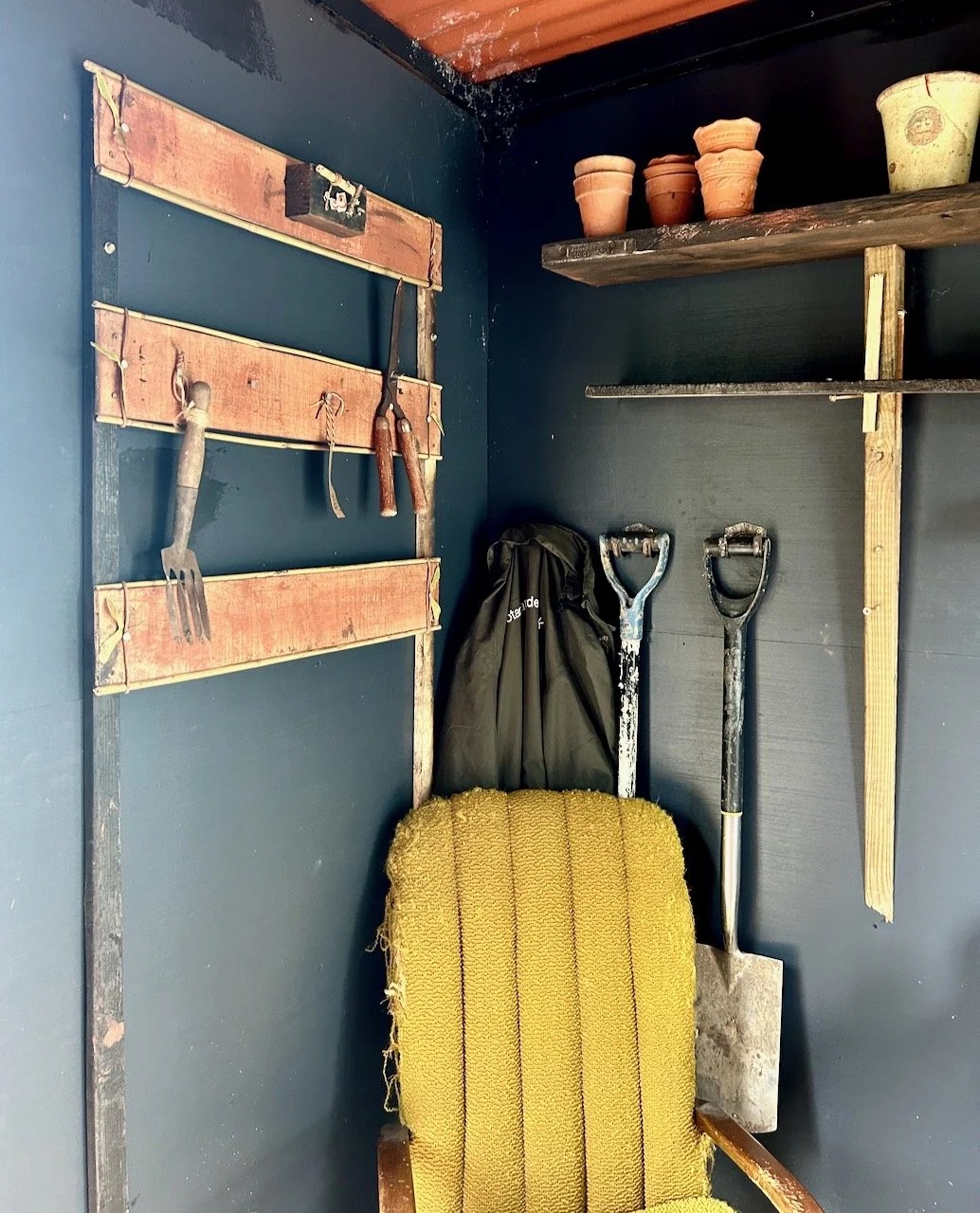 Black walls in the shed entrance to the garden with vintage tools and pots hanging on the wall/shelves