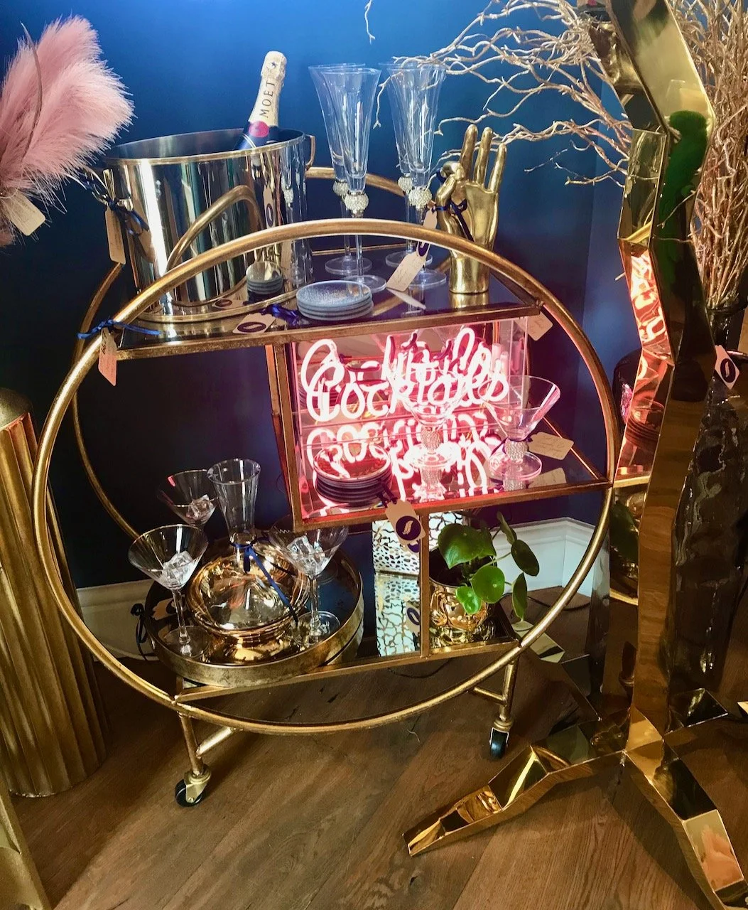 A circular drinks trolley with a champagne bucket, glasses and a neon sign saying cocktails