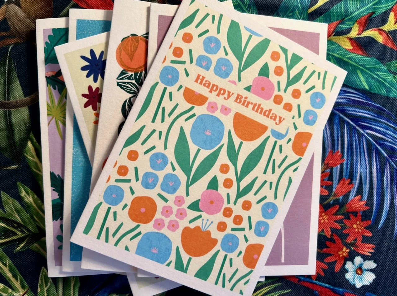 Cheery blue, orange and pink flowers on stems with leaves, with the happy birthday banner across them