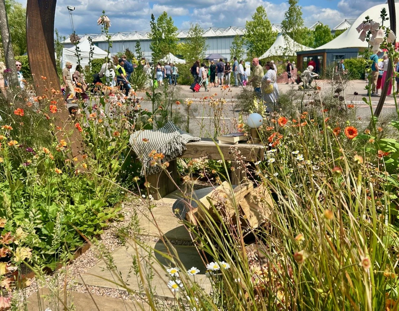 prairie style relaxed planting around the rusty metal arch which has a simple wooden bench beneath