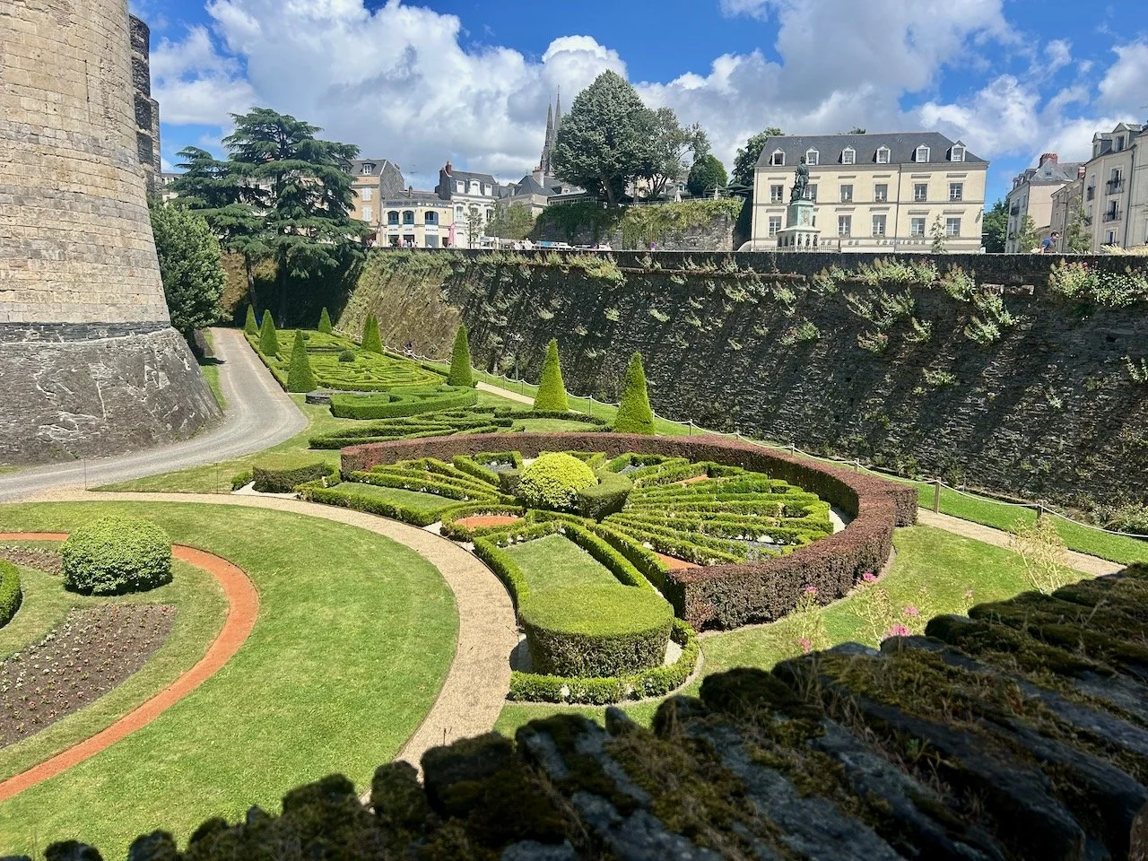the gardens and their parterre stretch around the corner of the castle's moat