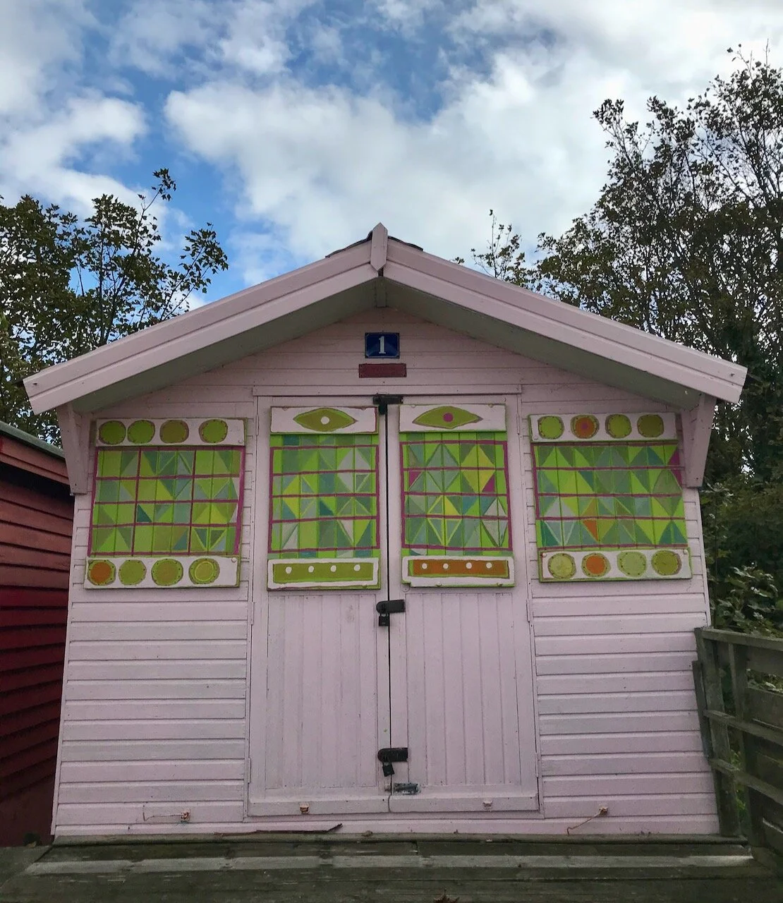a pale pink beach hut with geometric pattern in greens and yellows on the shutters