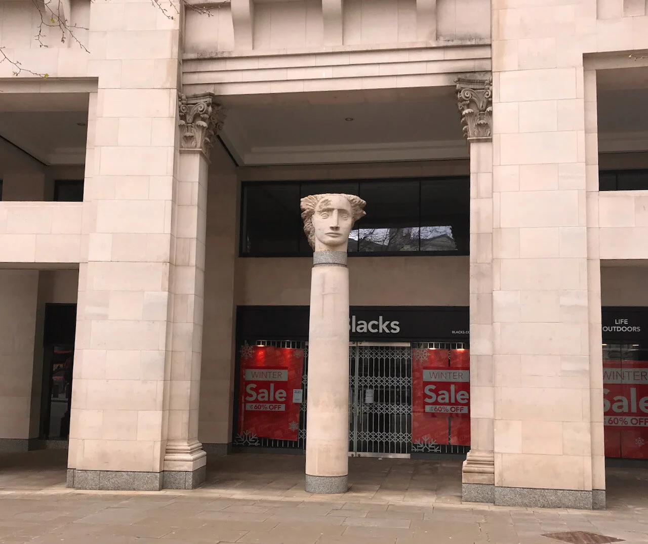 a sculpted head on a column with shops in the background.jpeg