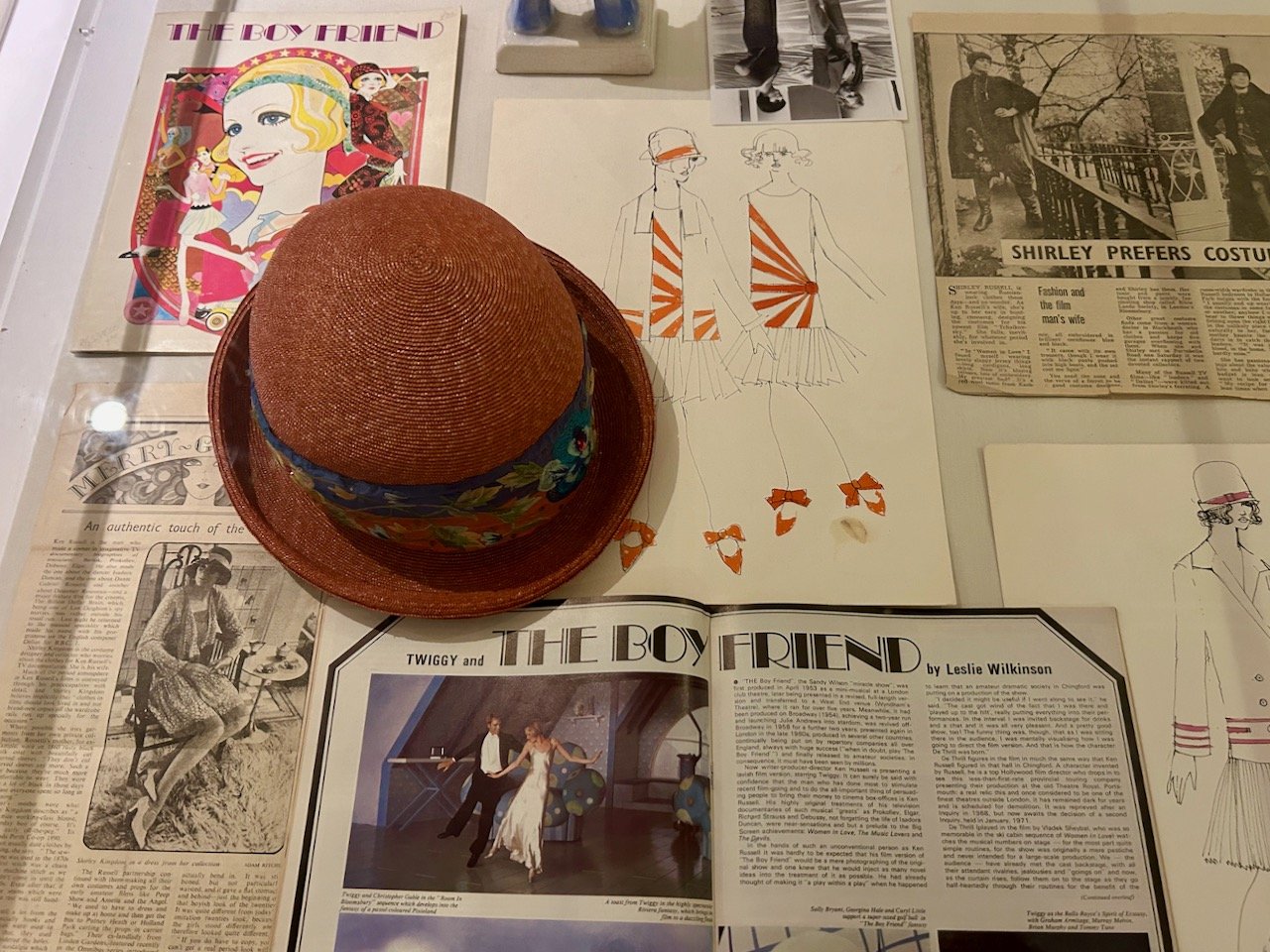 More memorabillia, a straw cloche hat, newspaper cuttings and in the centre a drop waisted dress/jacket combination which features a sunburst design on the waist, note the shoes - tied with ribbons too