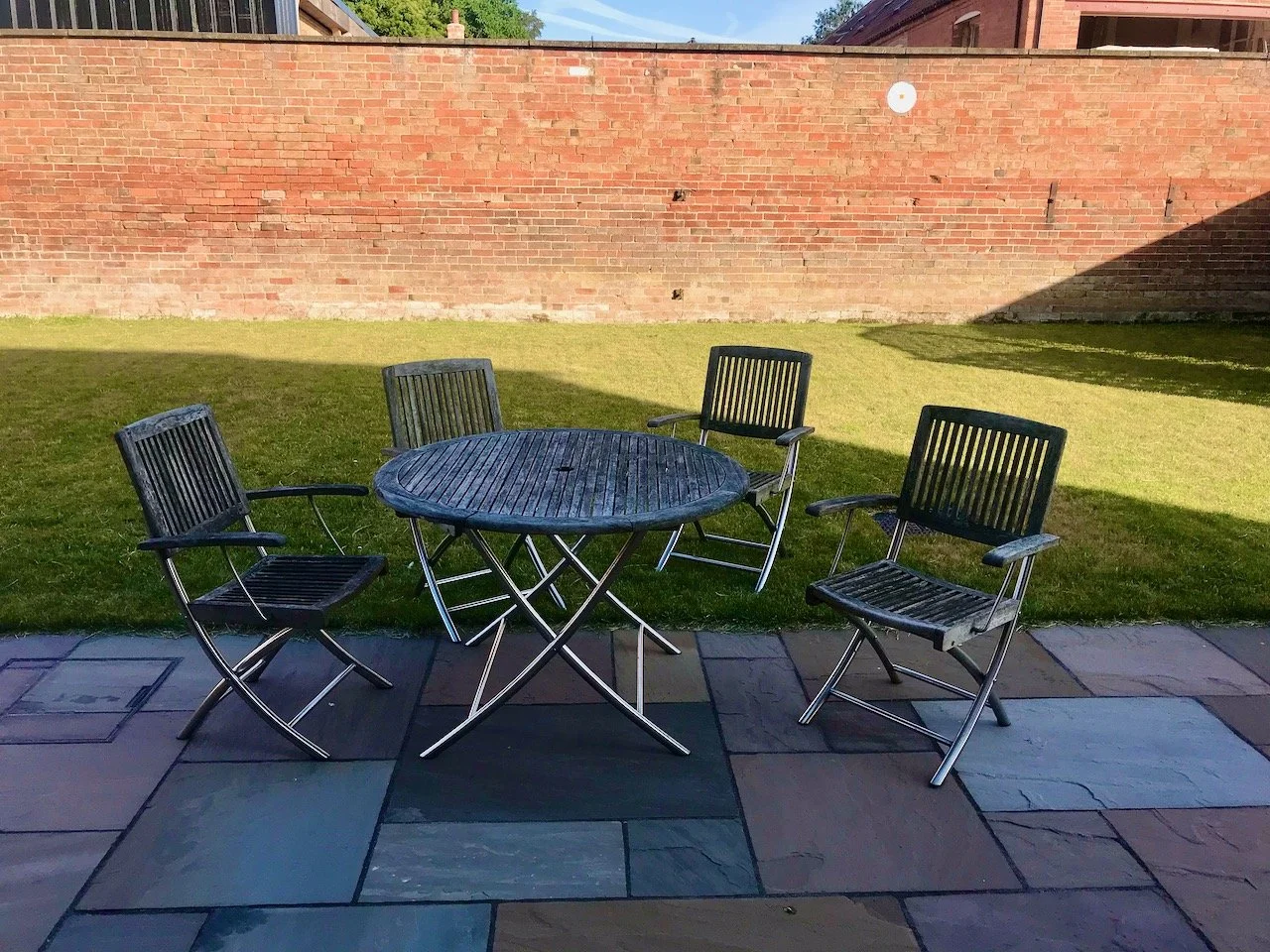 Looking out from our kitchen onto the patio and table and chairs, with the grass behind and the Grade II listed wall in the background