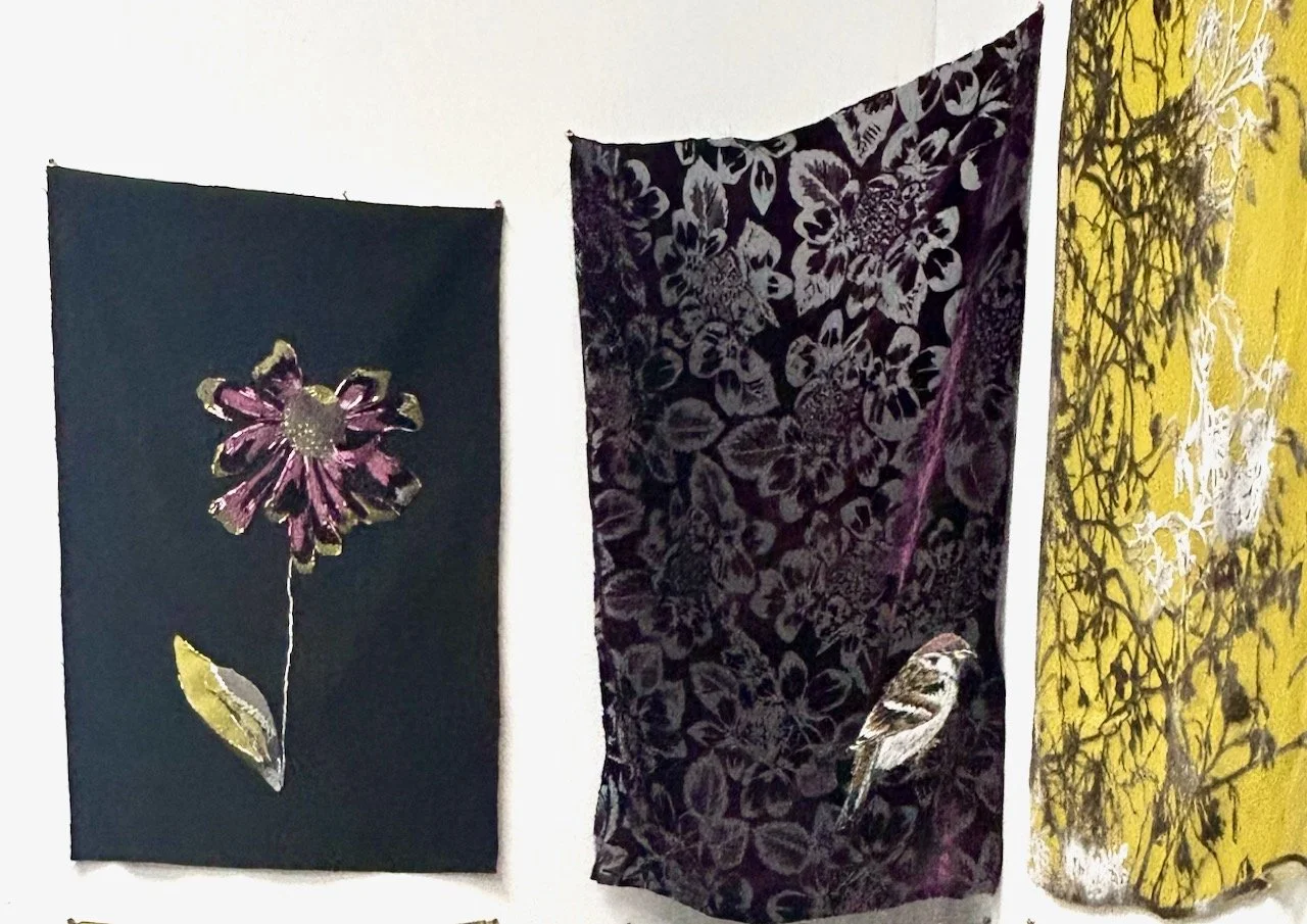 Three panels (one only part visible); from left - an embroidered flower on a plain background, an embroidered bird on a grey/black textured cloth and a yellow panel with branches embroidered
