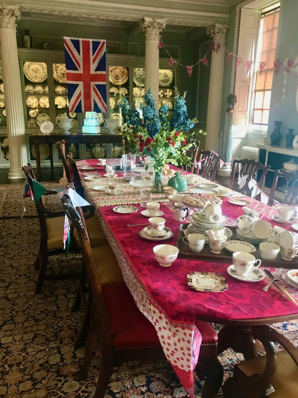 The dining room in the house laid for a jubilee tea party with a union flag hanging in the background