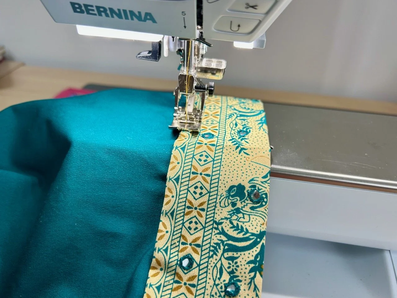 Sewing one of  the patterned bands to the plain teal fabric of the dressing gown
