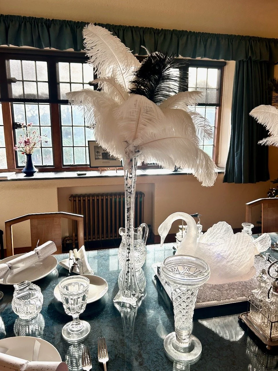 Glassware and crystalware set out on the dining table with black and white ostrich feathers in a tall vase as decoration