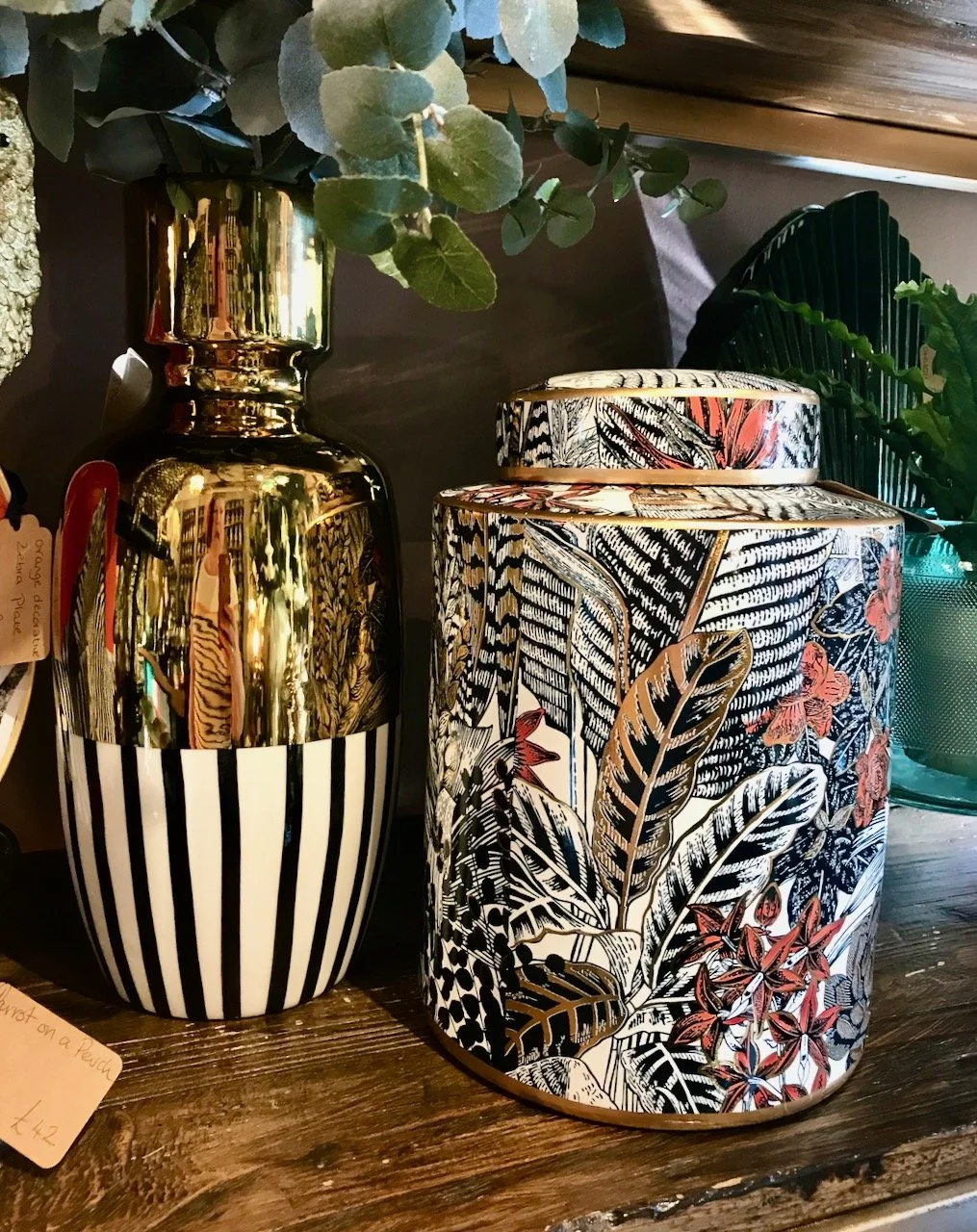 More pots, a taller/thinner pot with black/white vertical stripes and gold on the top next to a black white and pink leaf design lidded pot