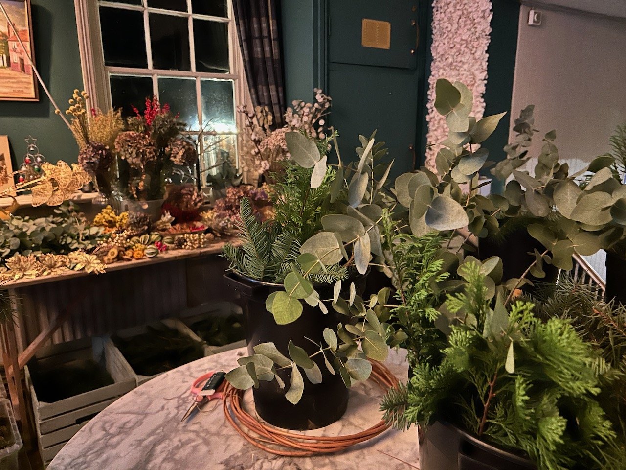 Buckets of greenery and willow rings in the foreground with a luscious table of decorations behind