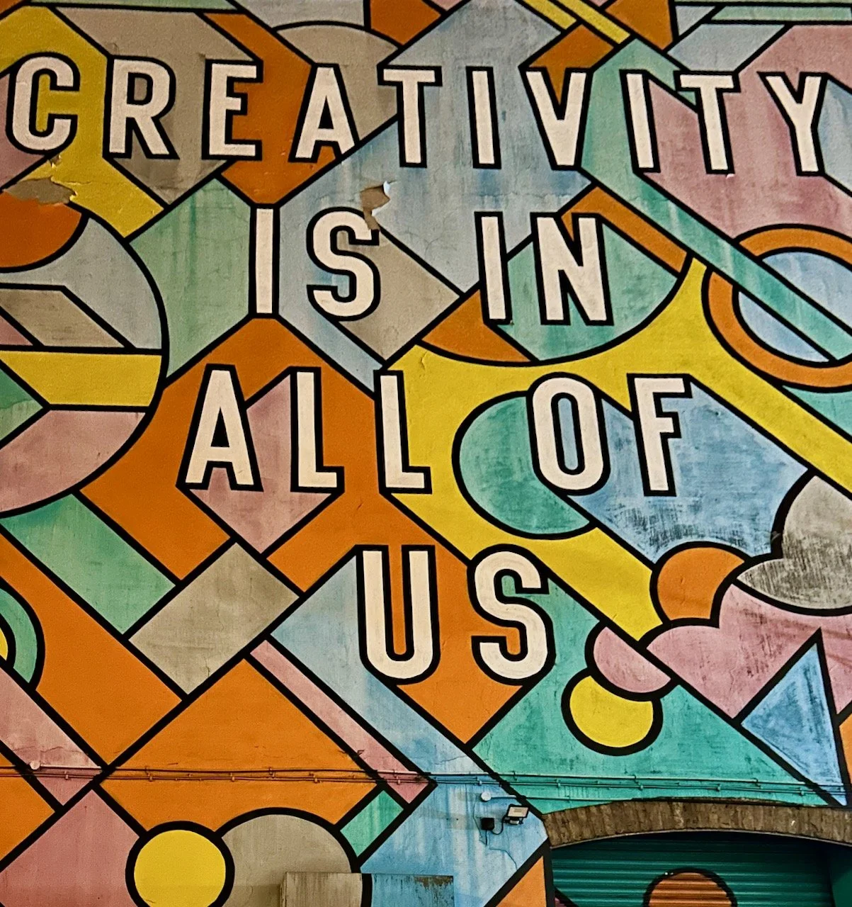 Creativity is in all of us - painted on the side of a building with a geometric colourful pattern behind