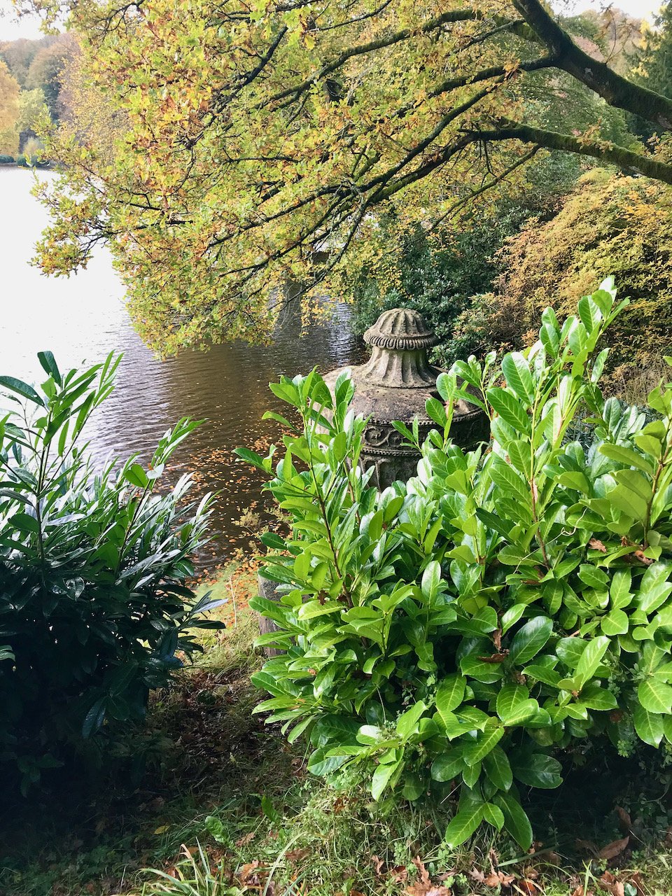 Looking down through bushes to the lake with an urn-like sculpture on the water's edge partially obscured
