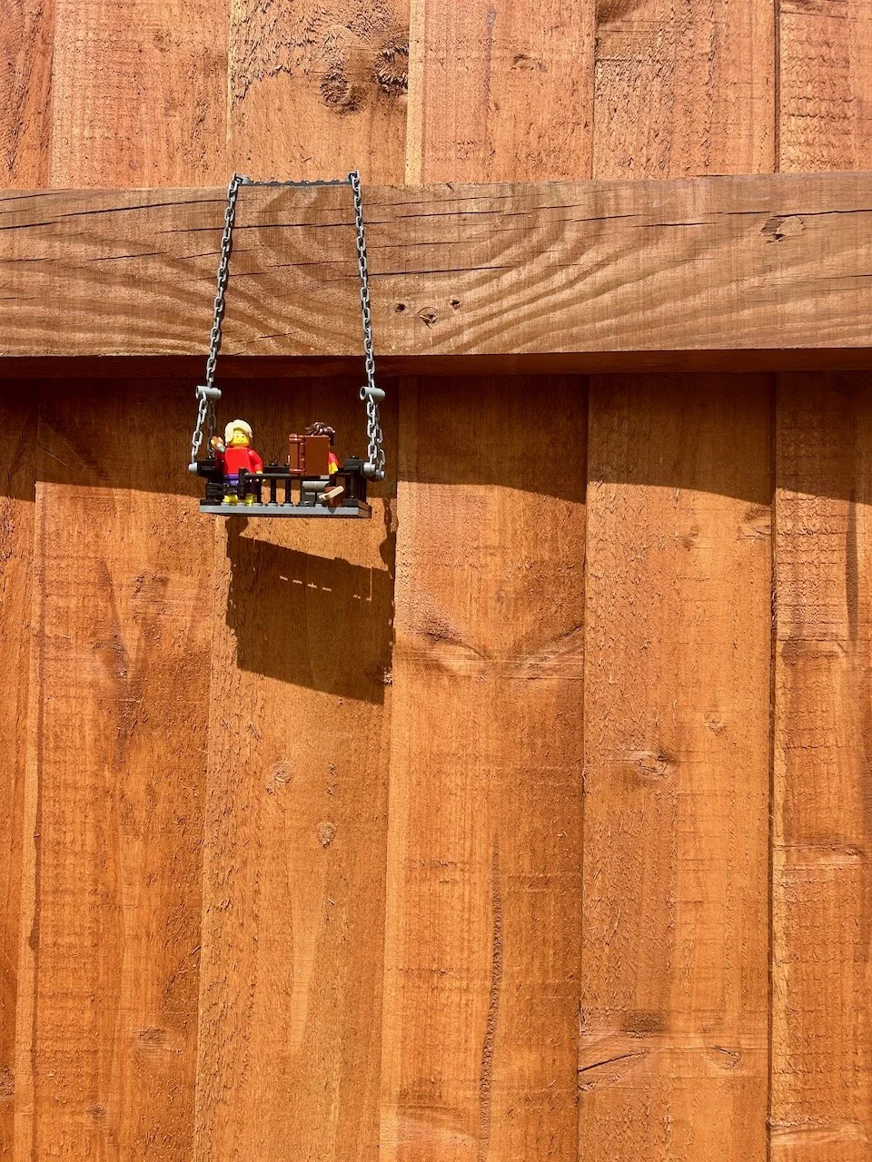 Two lego figures enjoying hanging from the fence -one's even reading a book!