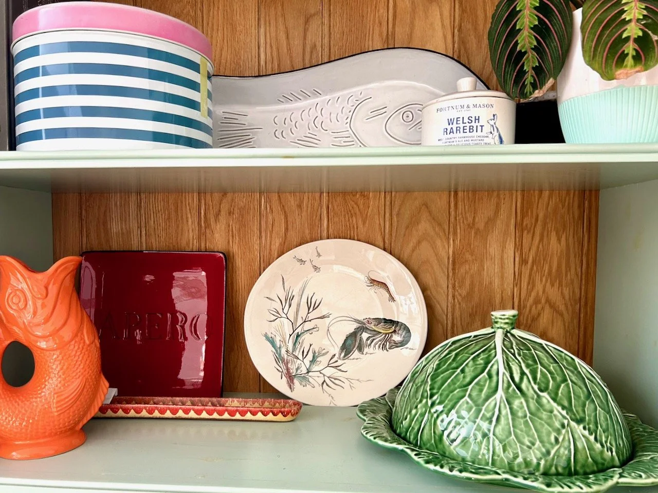 The new to us lobster plate on the dresser along with the guggle jug and cabbage platter with a joules striped tin, a fish dish a welsh rarebit ceramic tub and houseplant on the shelf above