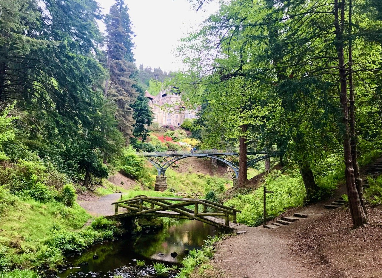 taken from the walk through the woods towards the house, with a wooden footbridge across water in the foreground, a larger iron bridge behind
