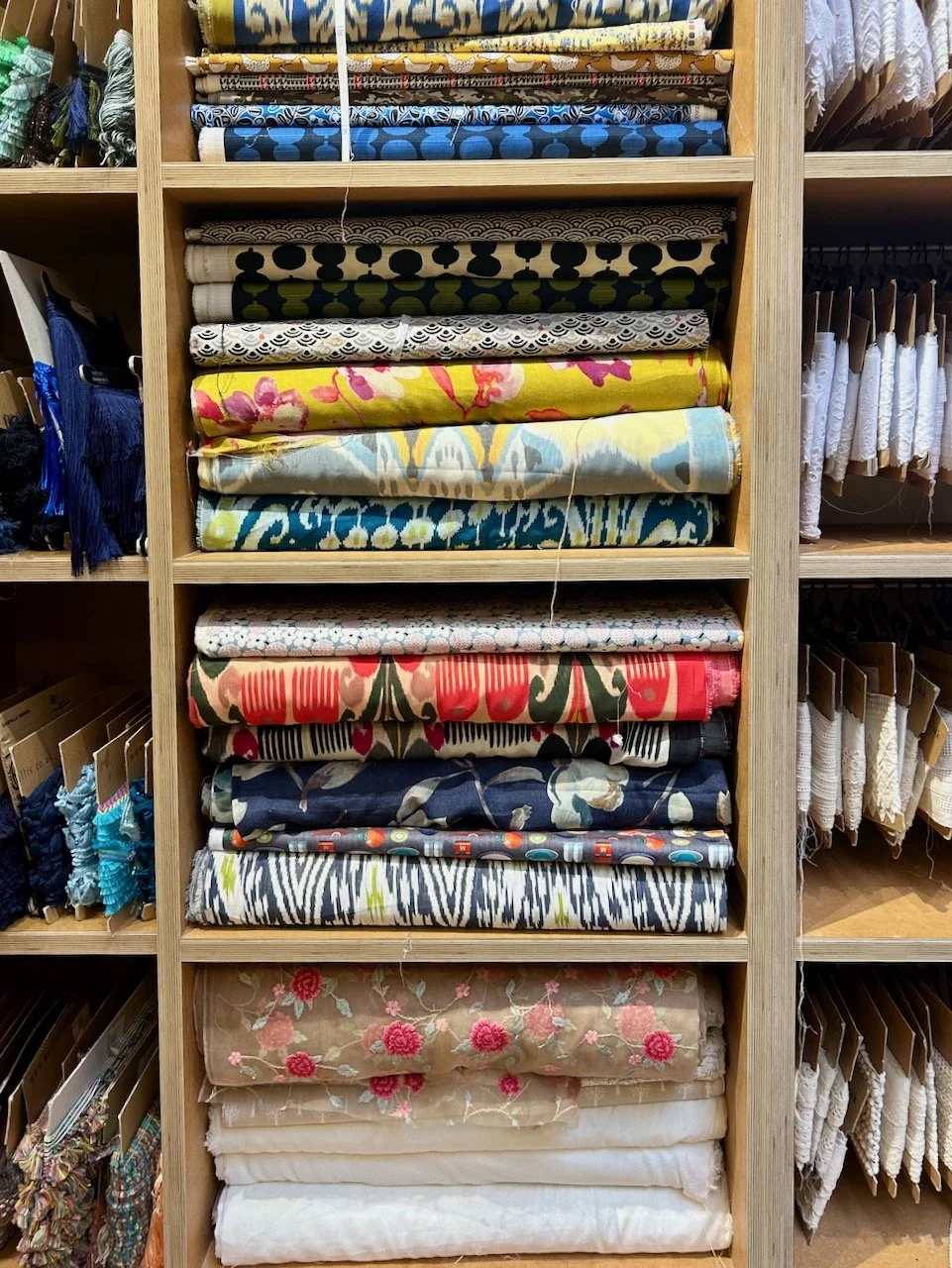 Bolts of fabric stacked on the shelves with lace and trimmings either side