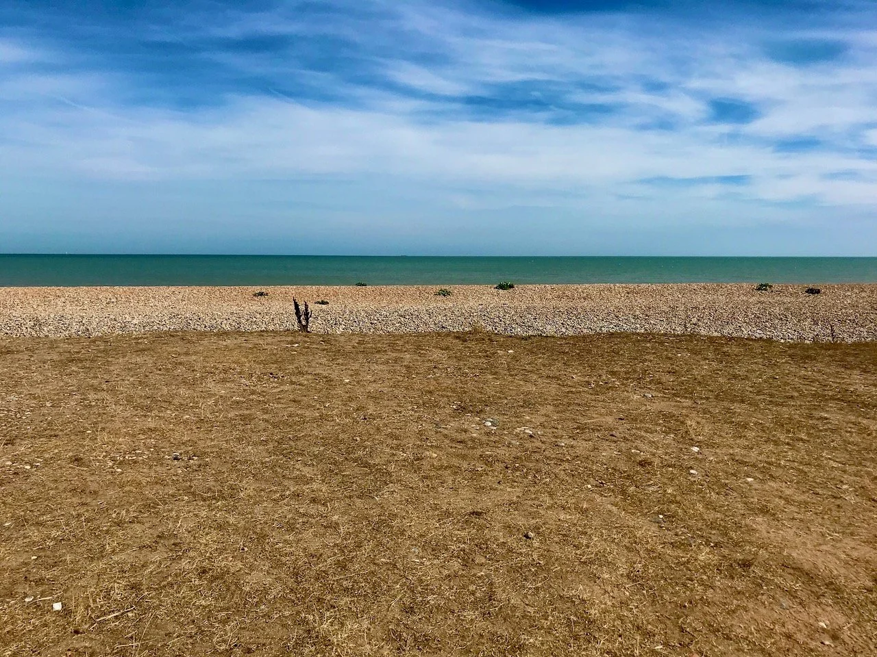 The stony beach, green sea and blue sky at Sandwich Bay, Kent