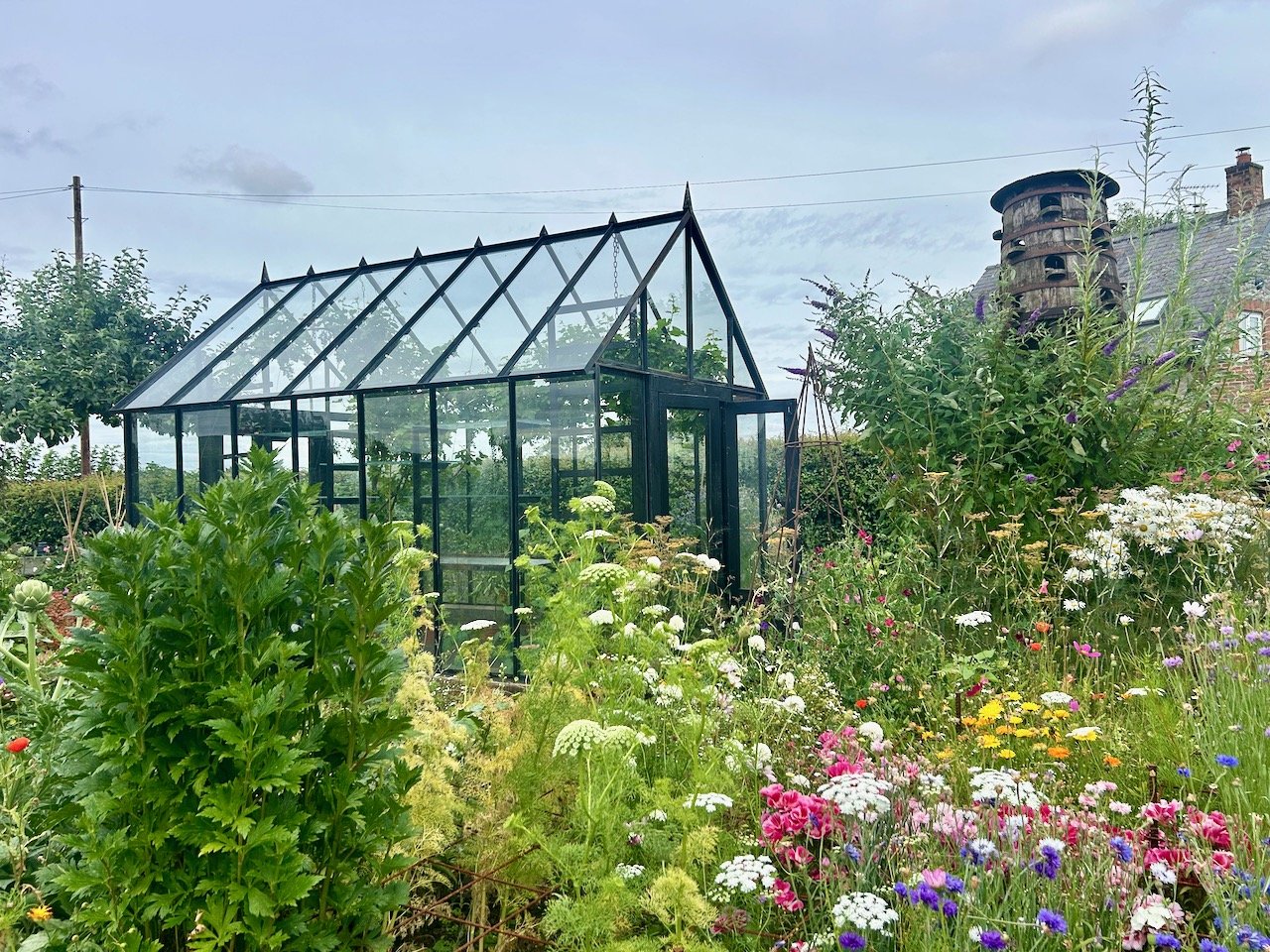 a lush colourful border and greenhouse (not mine) at Sibthorpe open gardens