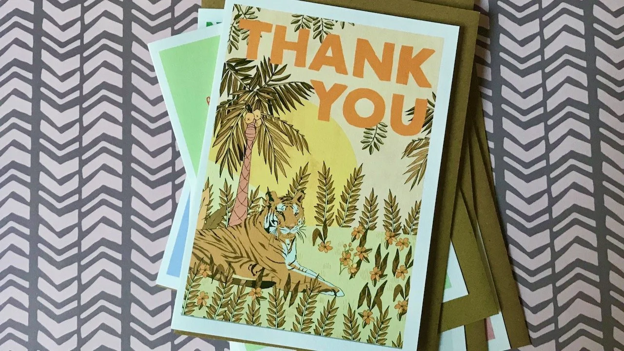 A tiger lazing among golden flowers, and palm trees with a yellow sun on the horizon.  The words 'thank you' in orange at the top of the card.