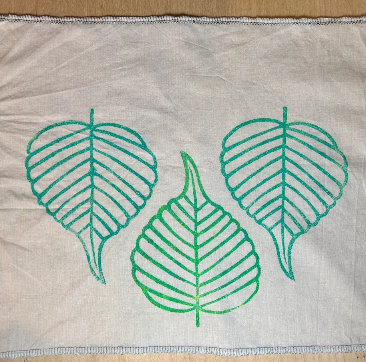 Three leaves block printed onto a piece of old bedding - two with the point down and a third between them with the point up