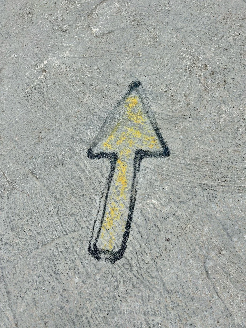 A yellow arrow edged with black pointing up - but is actually ahead, as this one was painted onto the ground