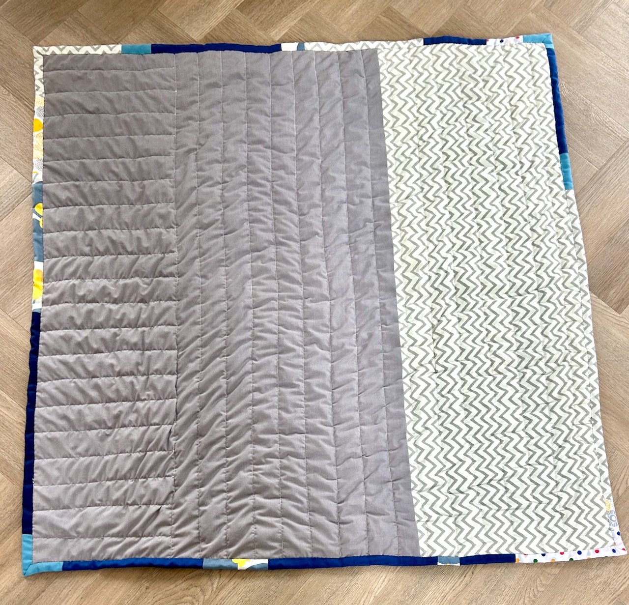 The reverse of the finished quilt - 2/3 grey, 1/3 grey/white chevrons. 2/3 quilted vertically, 1/3 quilted horizontally.
