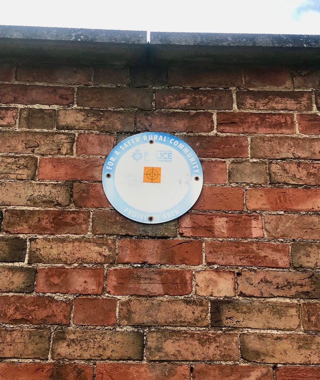 A Nottinghamshire Police round faded metal sign on the wall which says ' for a safer rural community protected area'