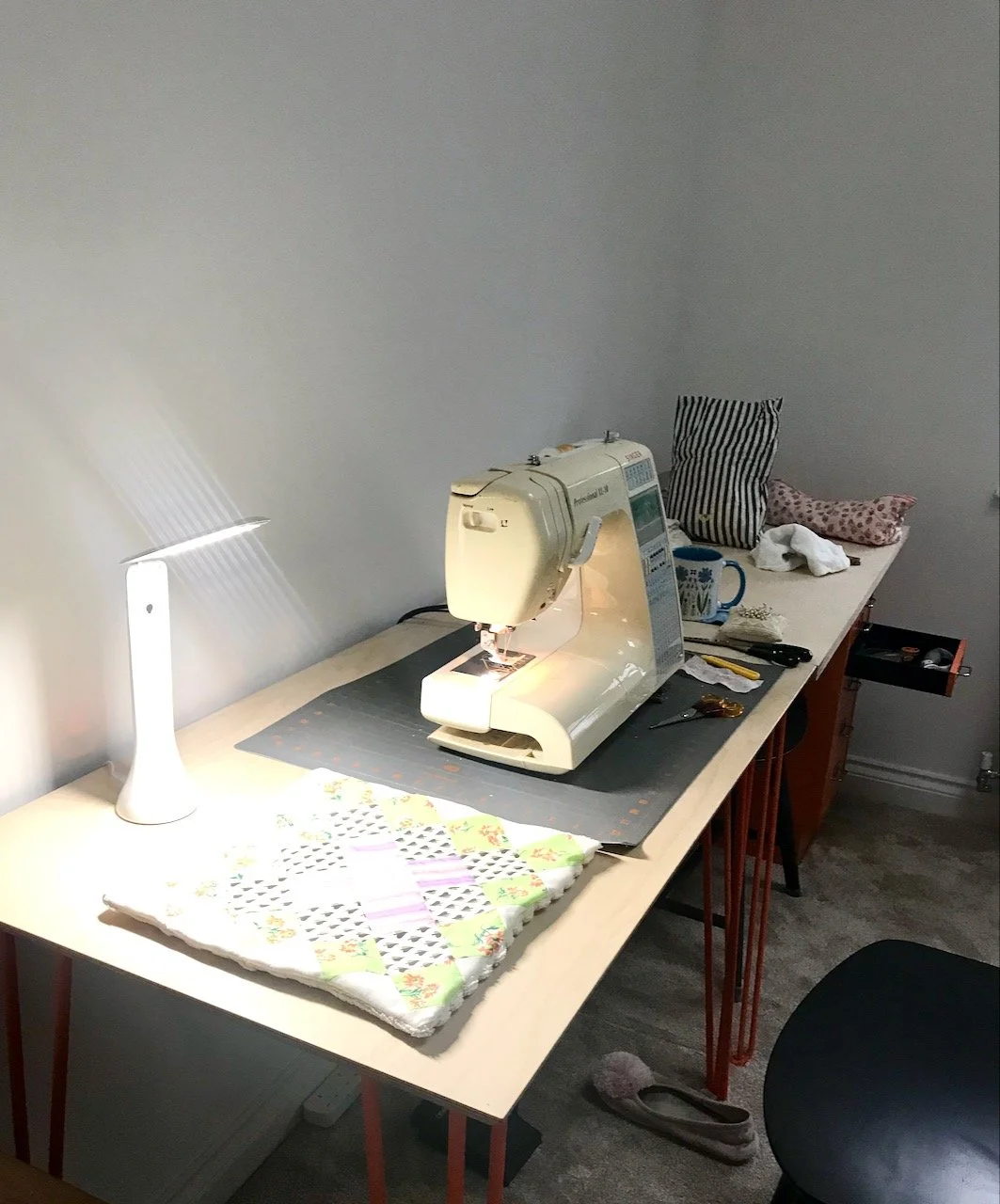 Sewing machine out, light on the end of the desk along with a completed kitchen towel, cup of tea to the right of the sewing machine and slipper discarded in front of the stool, and a drawer open in the background - a craft room in use!