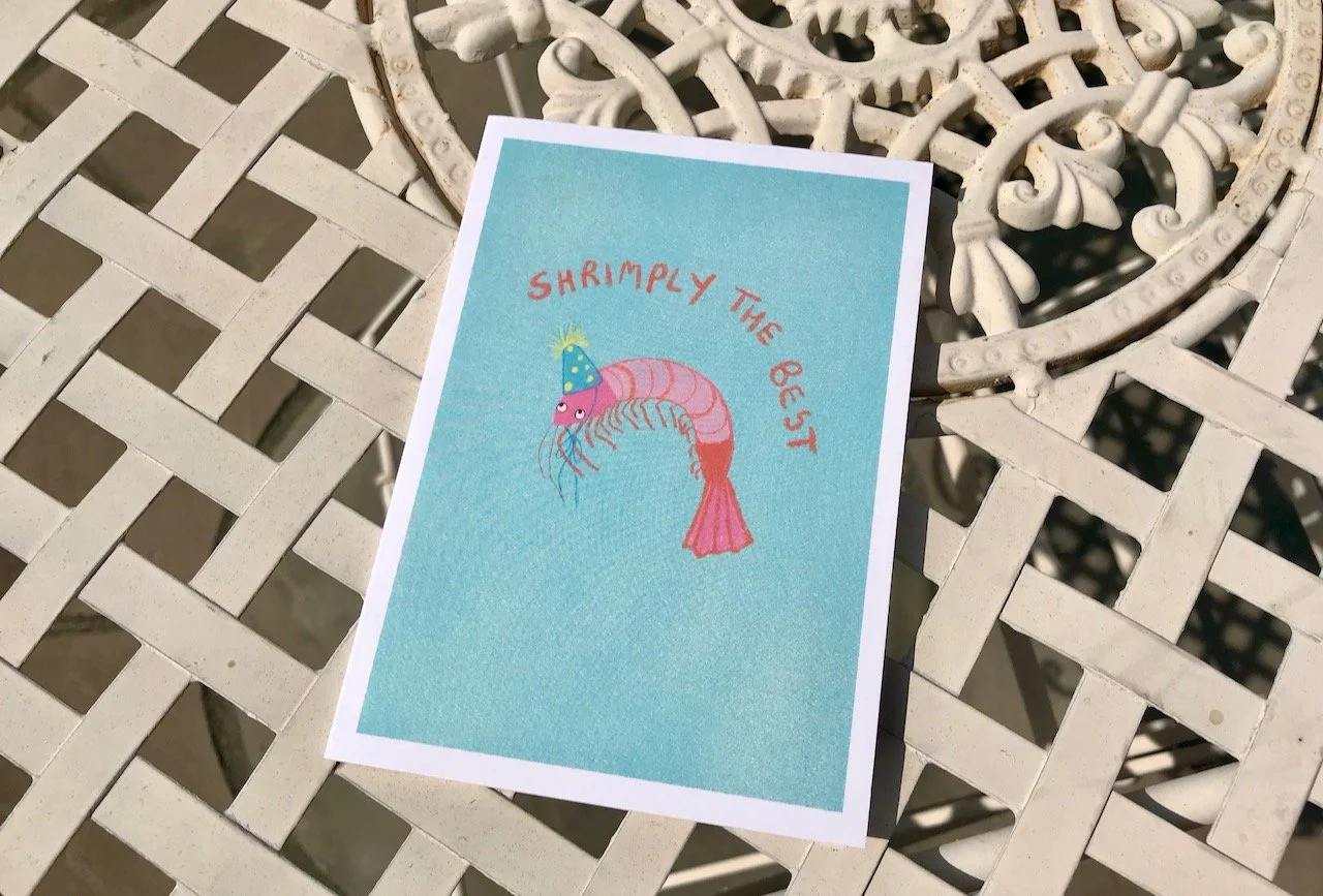 A blue card with a prawn wearing a party hat - the wording shrimply the best above