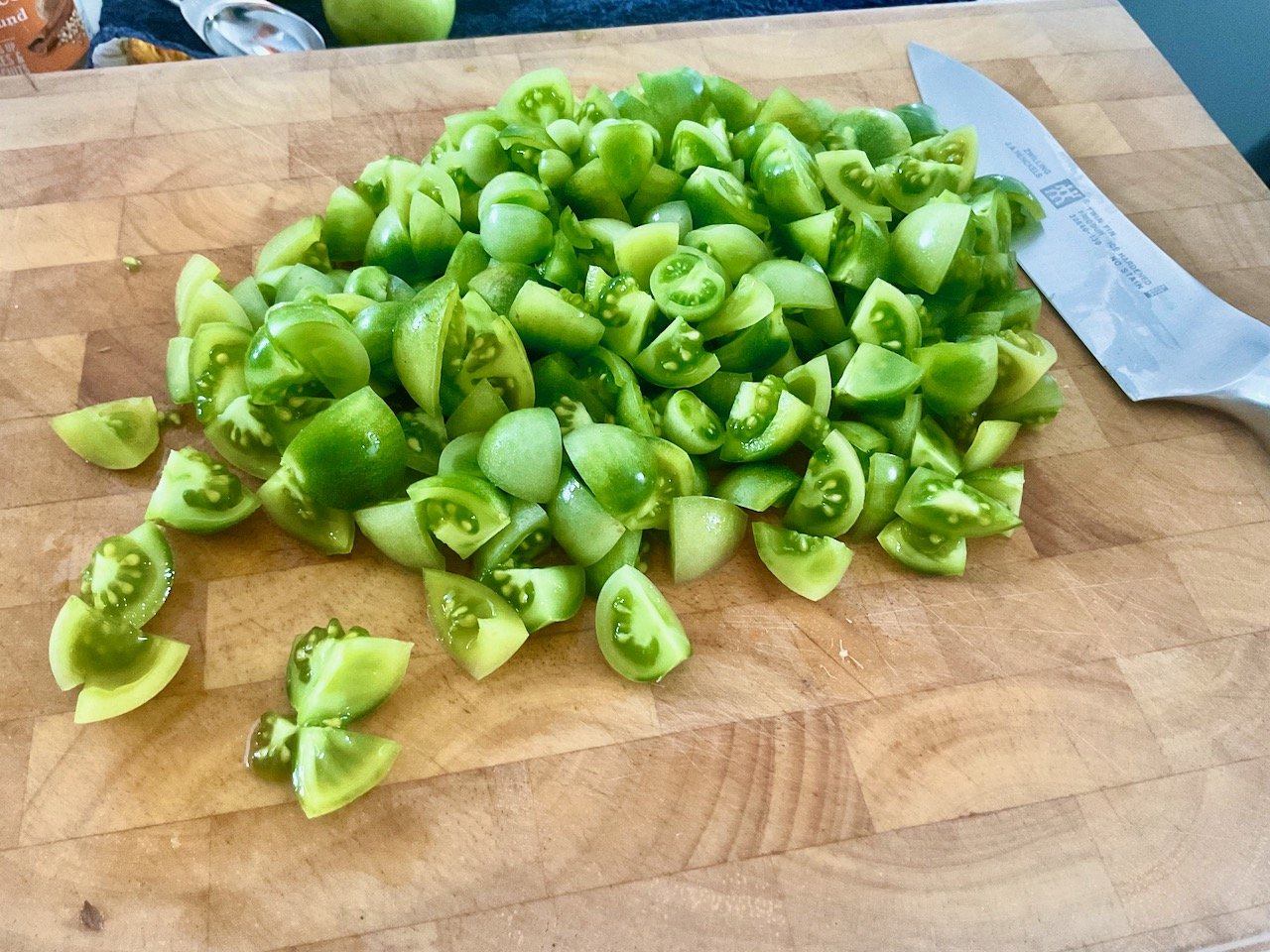 Young, fresh green tomatoes quartered on a wooden chopping board