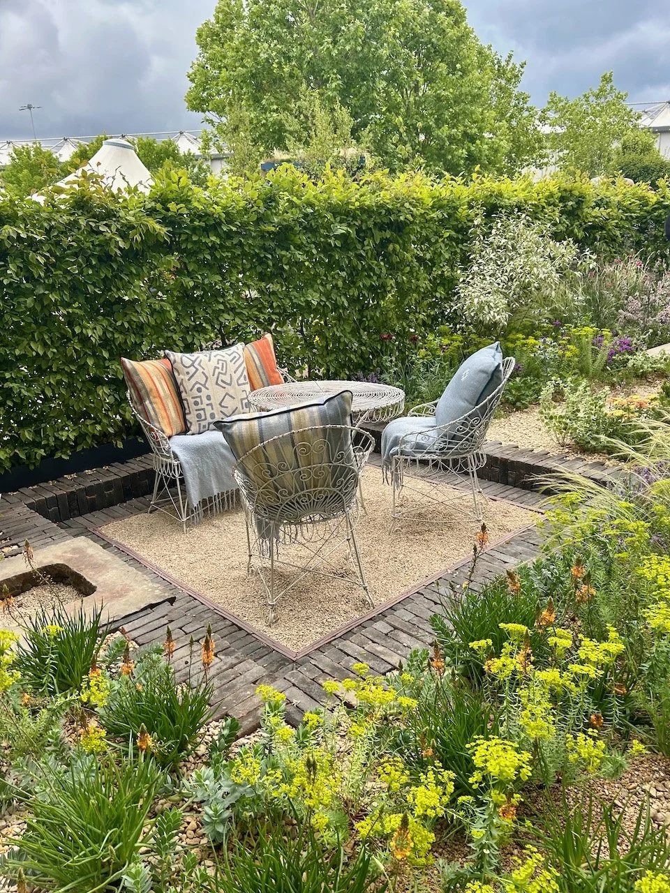 The slightly sunken seating area, edged with dark bricks and surrounded by planting including splurge and red hot pokers