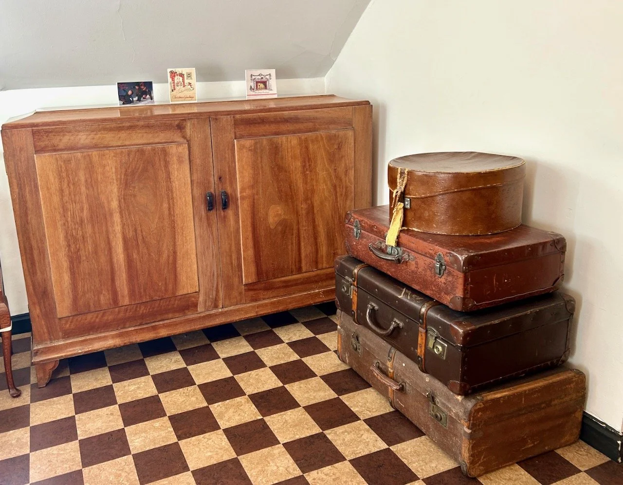 A stack of four vintage suitcases on a checkered floor with a wooden storage unit
