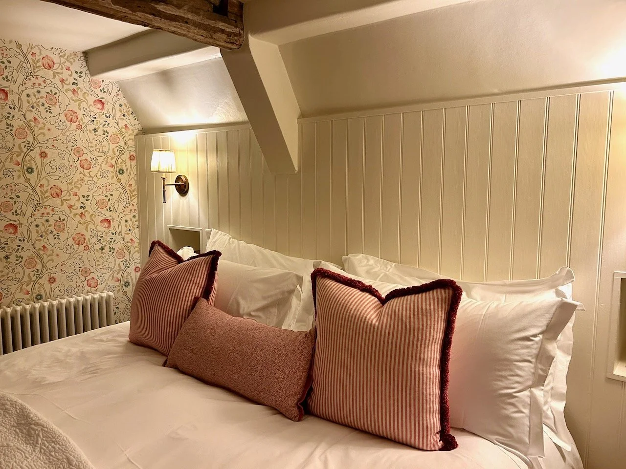 The bed with cushions and pillows, panelling behind and country style wallpaper on the walls