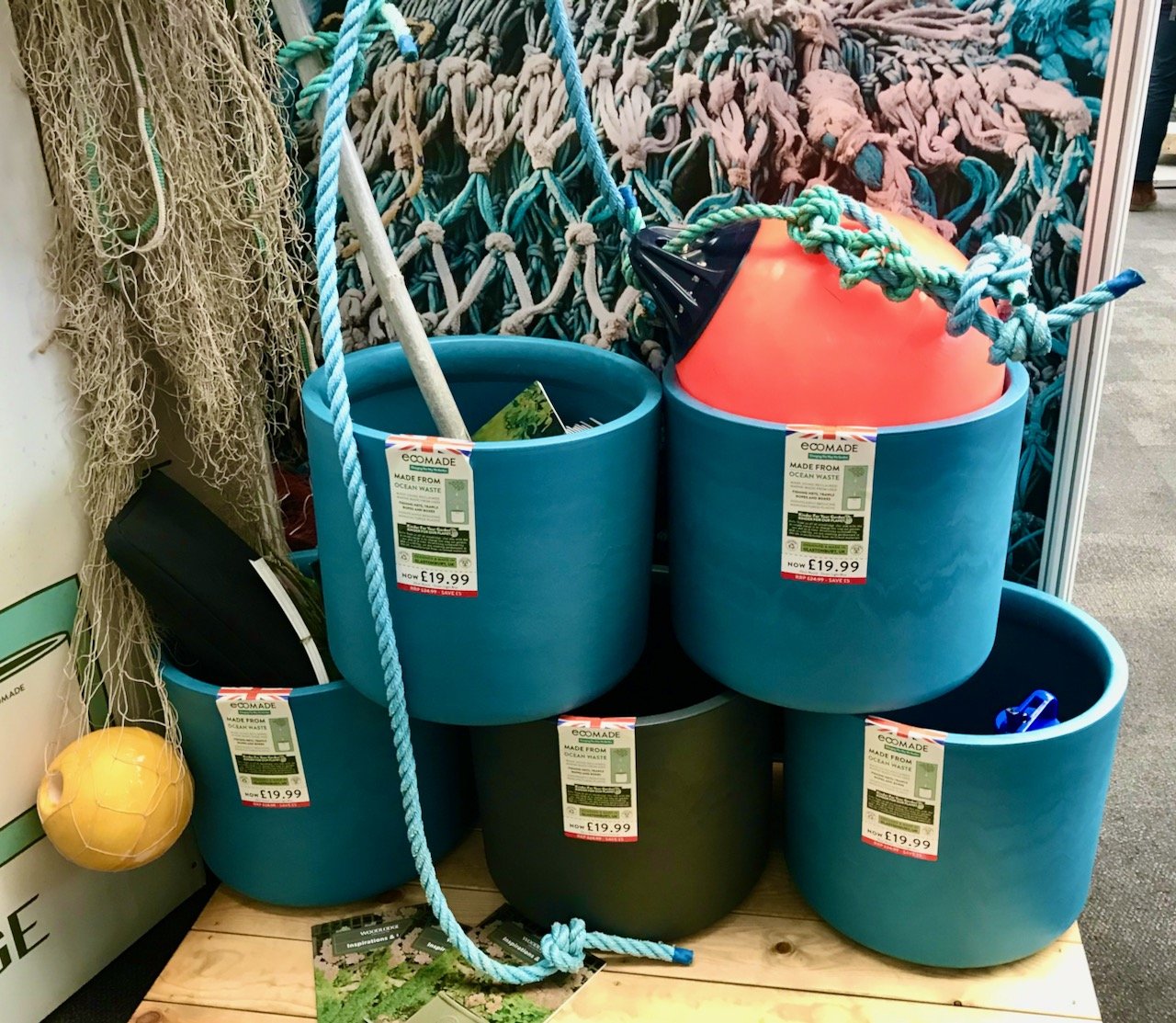 Five pots, 4 blue, 1 black, stacked on a display with a fishing nets behind and buoys