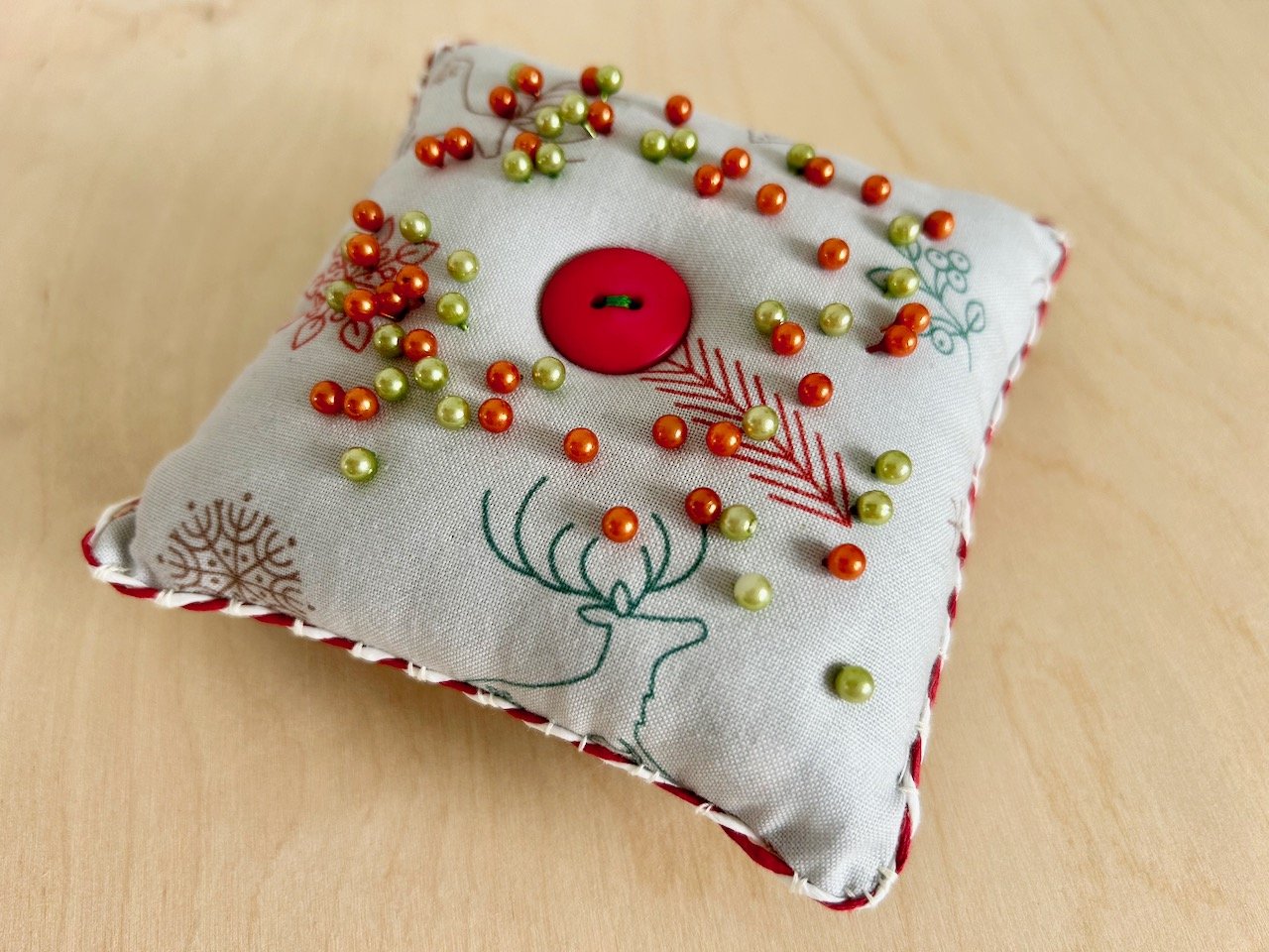 the same pincushion as the previous photo, now with orange and green pins pressed into the top and a red and white trimming around the seamed edge