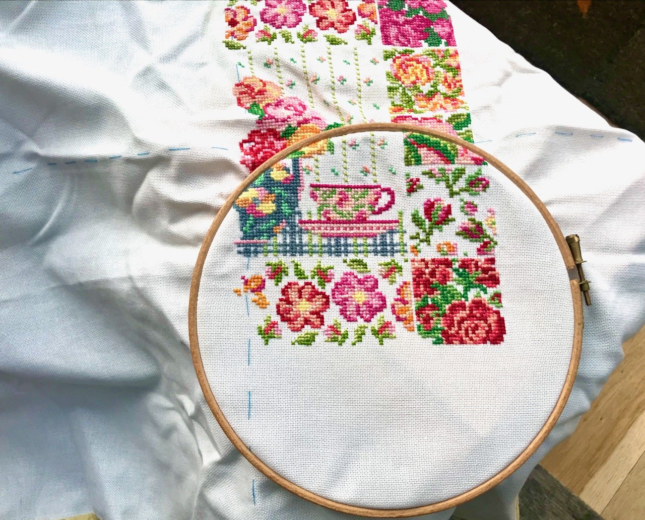 brightly coloured roses in cross stitch on a white background with some of the pattern contained within an embroidery hoop