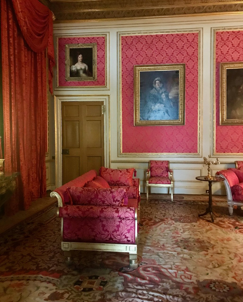 red wallpapered panelled sections with portraits in the drawing room, with wallpapers and curtains i nthe same pattern and an ornate (and large) carpet