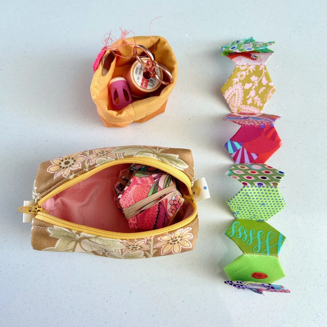 A selection of hexies secured with elastic bands, a mini pouch, needle thread, scissors and a thimble