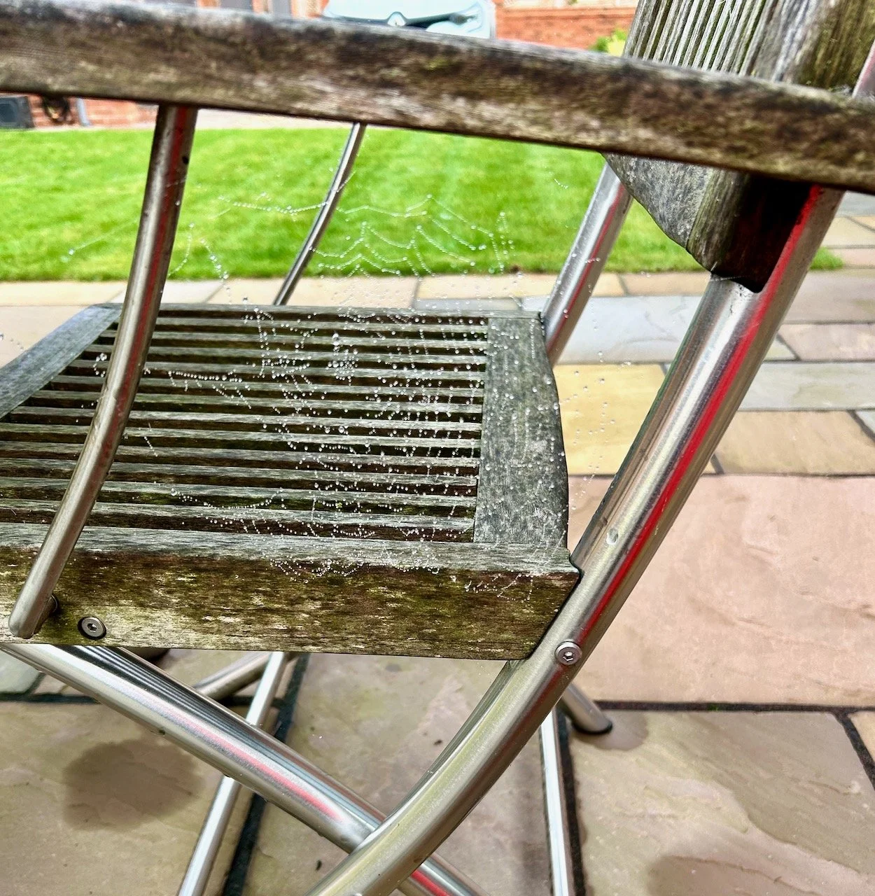 A dew covered spider's web under the arm rest of the garden chair