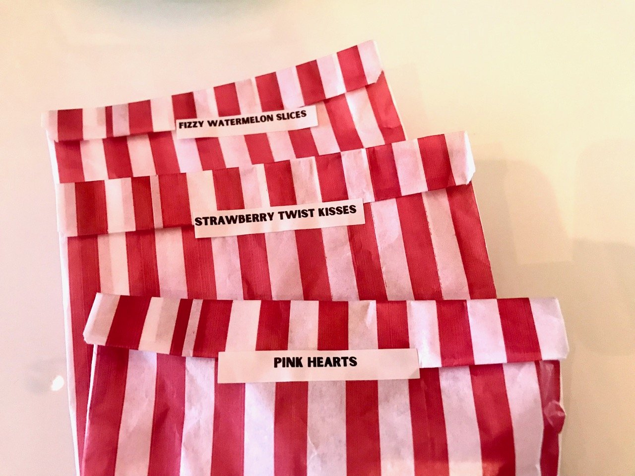 Three of the red and white striped bags containing Fizzy watermelon slices, strawberry twist kisses and pink hearts
