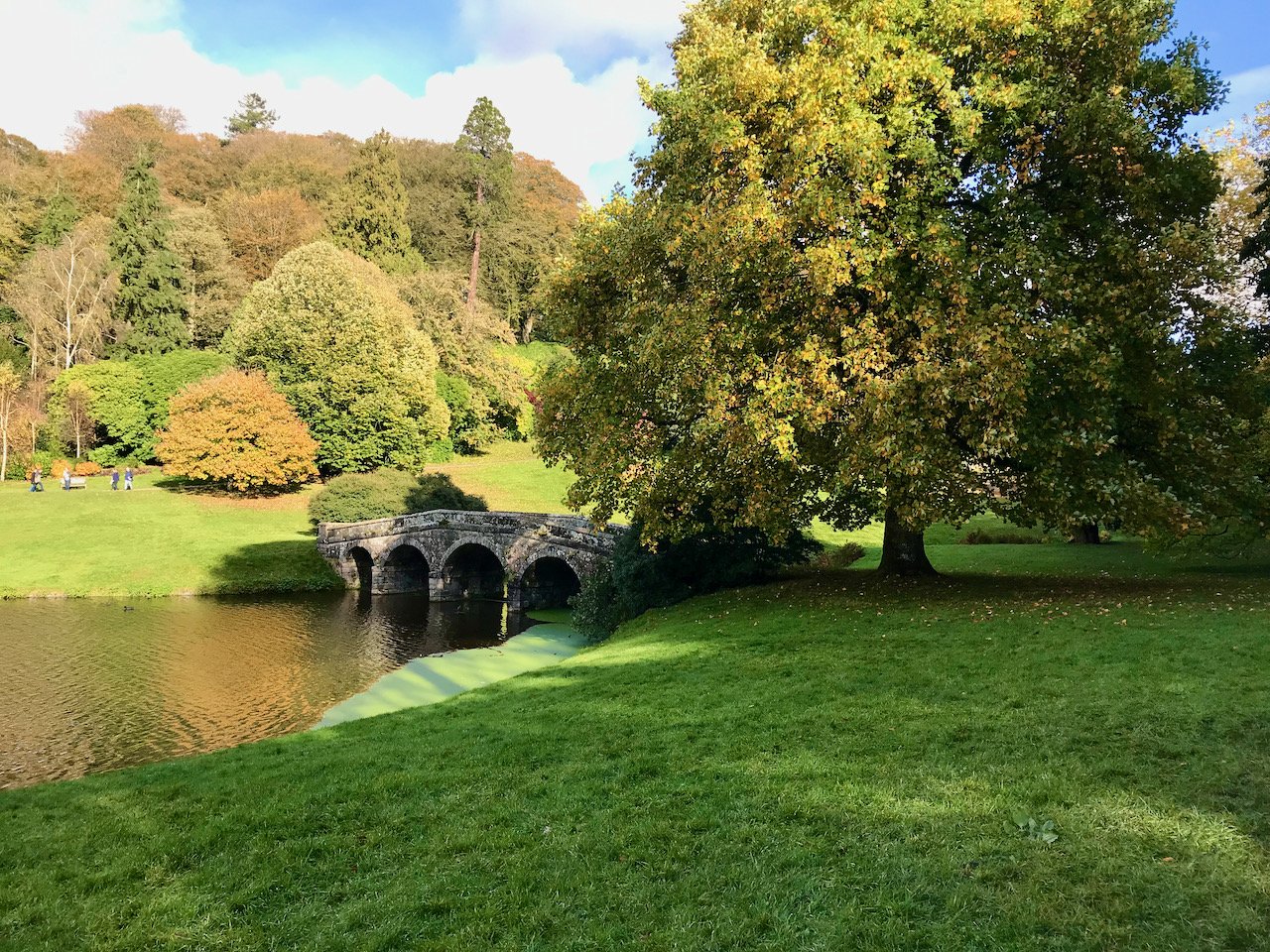 a usual view of stourhead with the arched bridge over the lake autumnal colours with the sun shining