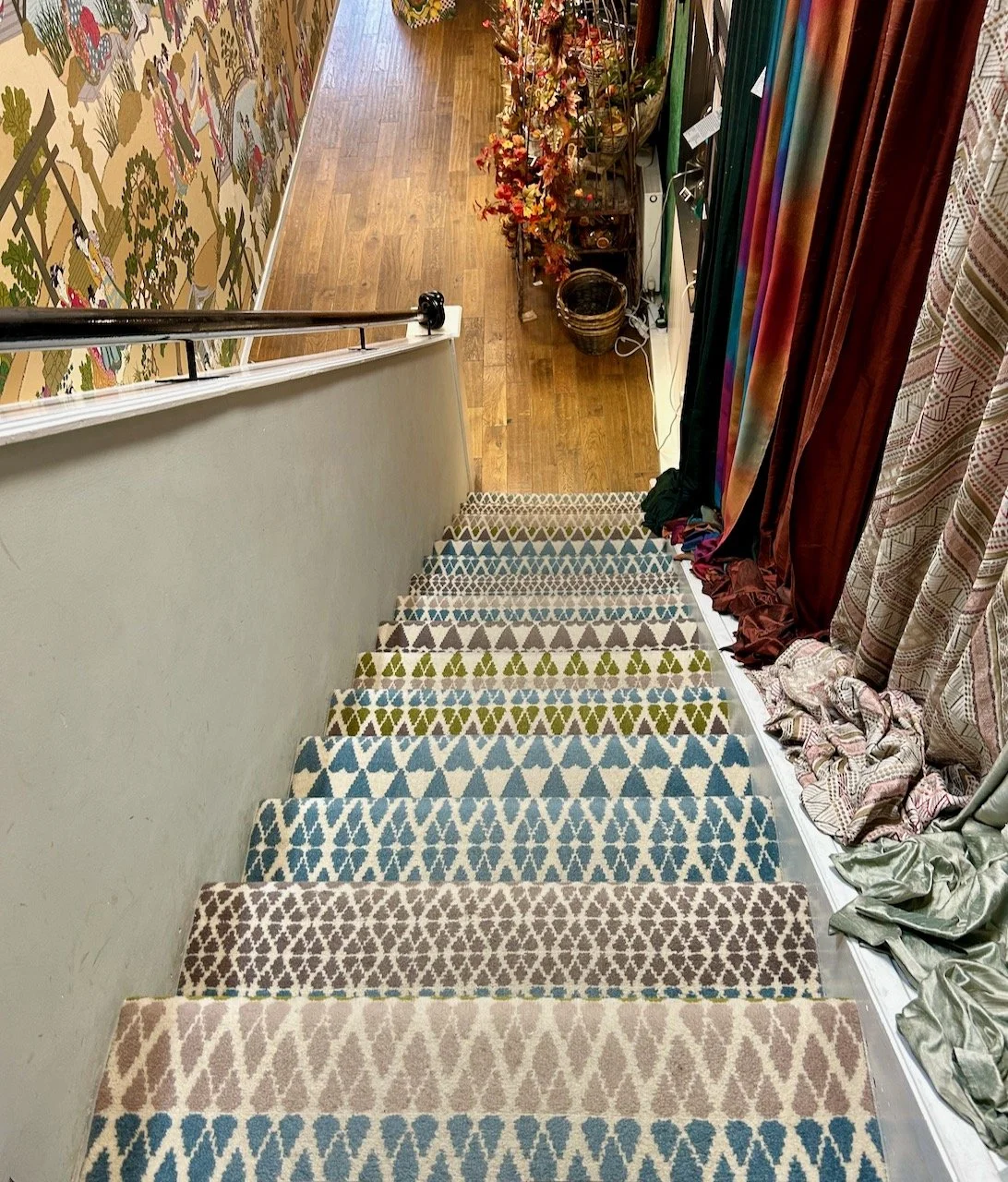 Looking down the stairs at the carpet which is a mix of repeating patterns on each step with blues, beige and greens