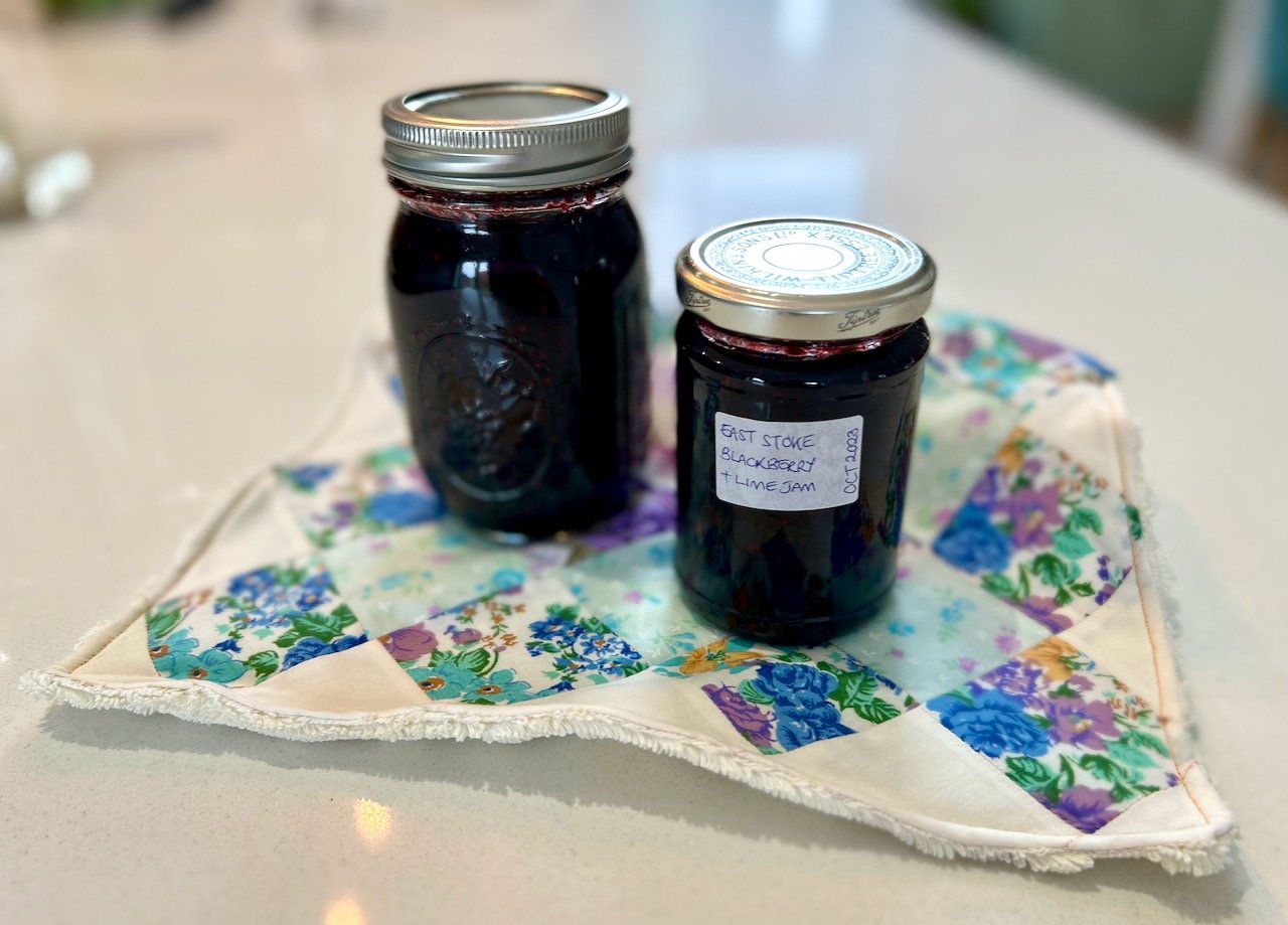 Two jars of homemade 'East Stoke Blackberry & Lime Jam' in my kitchen displayed on a patchwork home sewn reusable kitchen towel