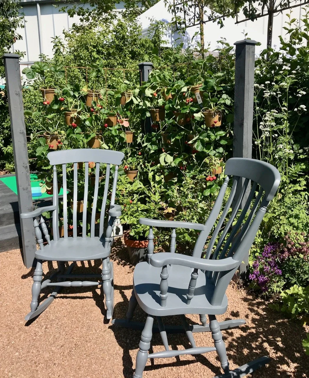 Two wooden rocking chairs painted grey set on gravel in front of the border