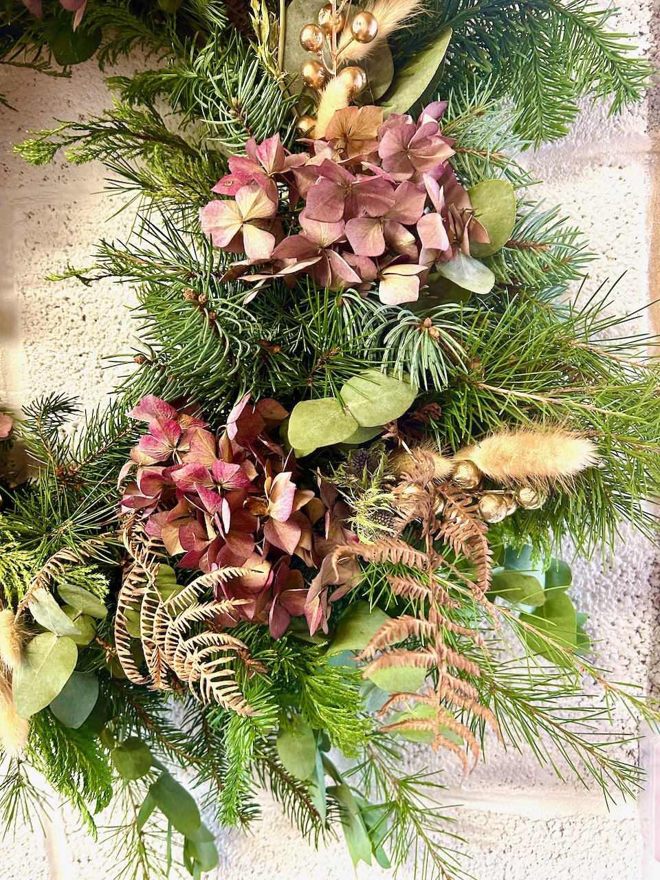 A section of the wreath with dried pink hydrangeas, dried bfacken and golden balls along with pale fluffy  grass heads