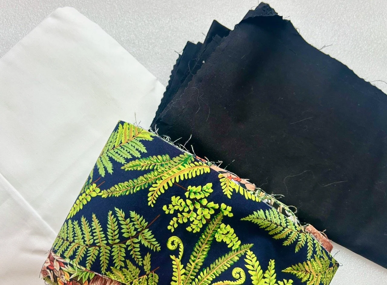 White and black fabric, with fern fabric offcuts in the foreground