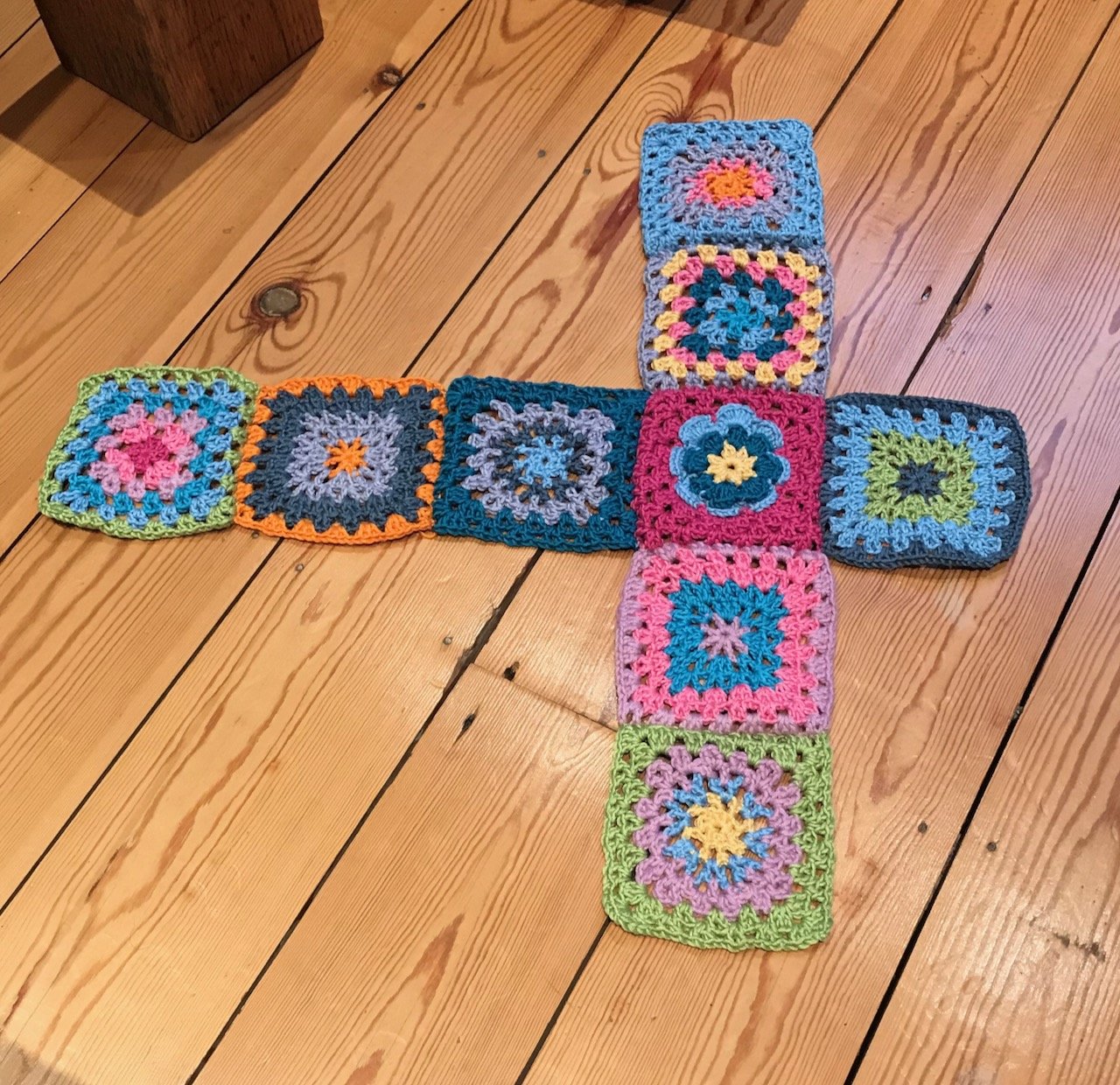 9 brightly coloured crocheted granny squares on a wooden floor