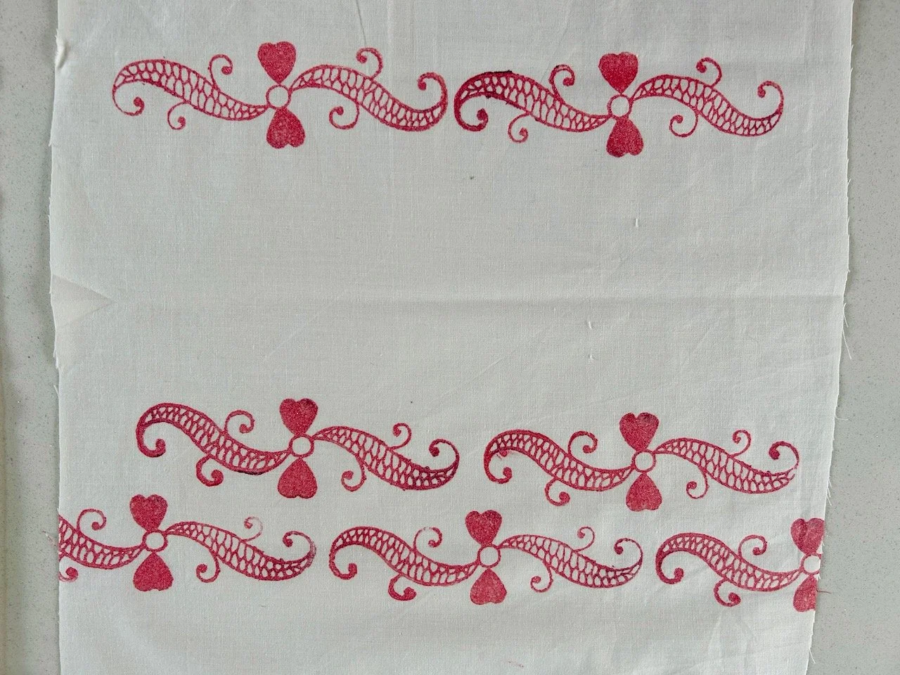 Three rows of indian block printed swirl patterns, pink on a cream background